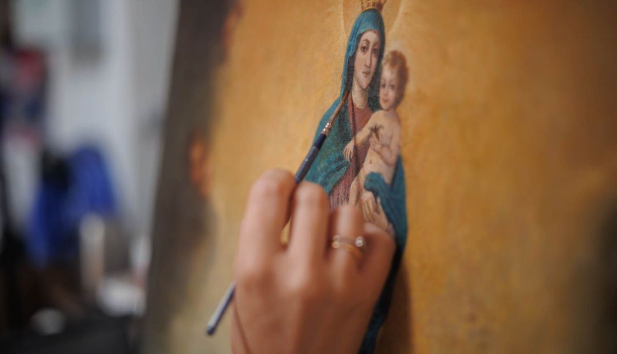 La man de la restauradora trabajando sobre un óleo.