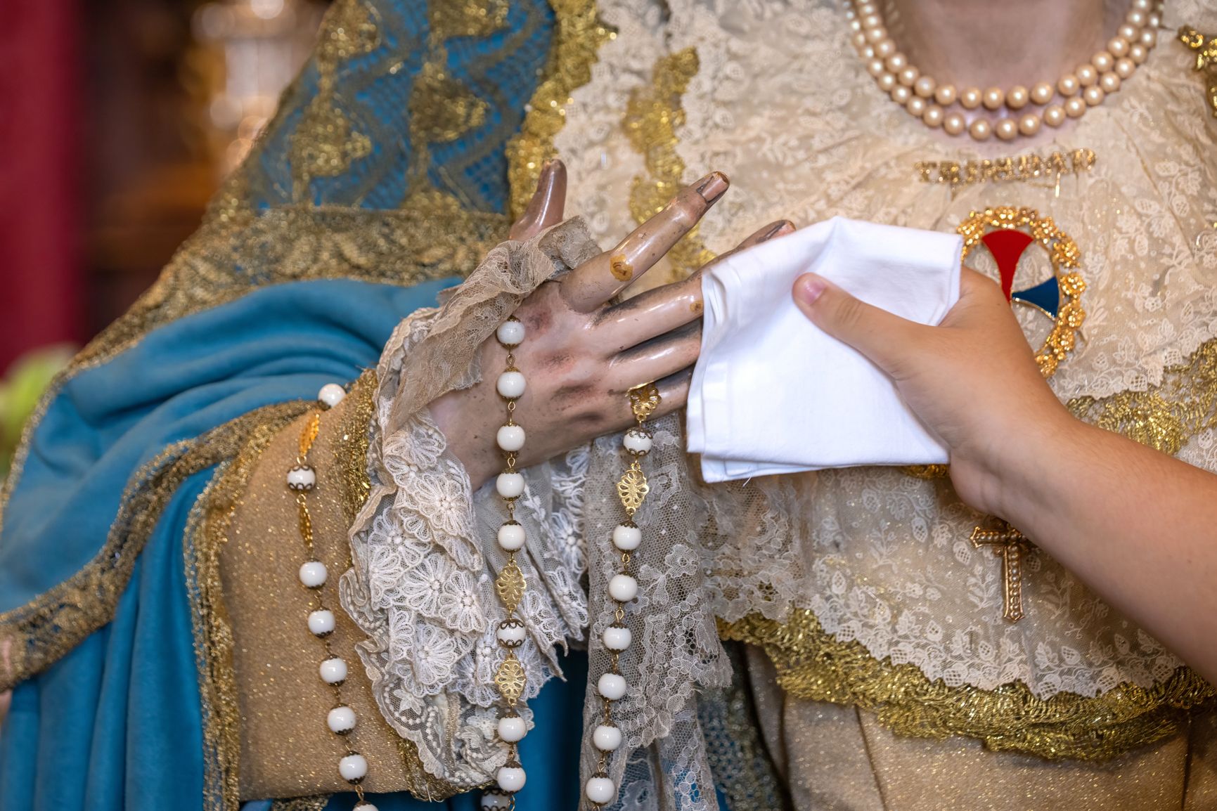 Una persona limpia las manos de la Virgen tras besarlas.