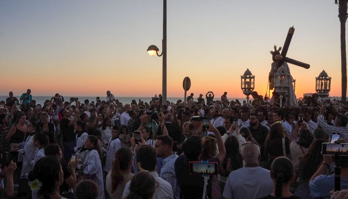 Centenares de personas junto al Señor, en un contraluz con la puesta de sol sobre el mar. 