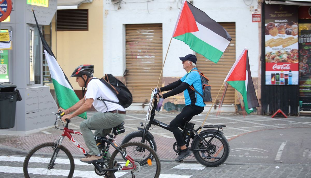 Dos hombres en bicicleta, portando banderas de Palestina.