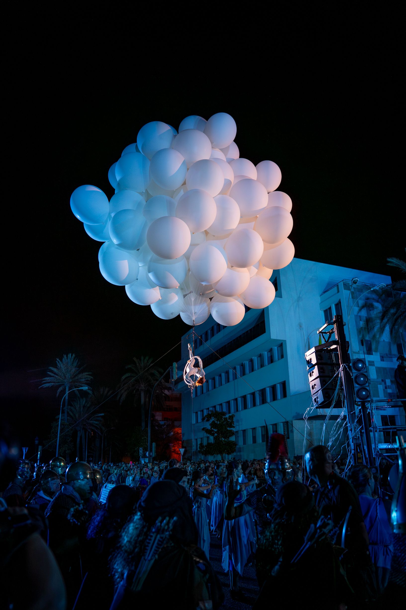 Una bailarina, suspendida de globos blancos sobre el público.