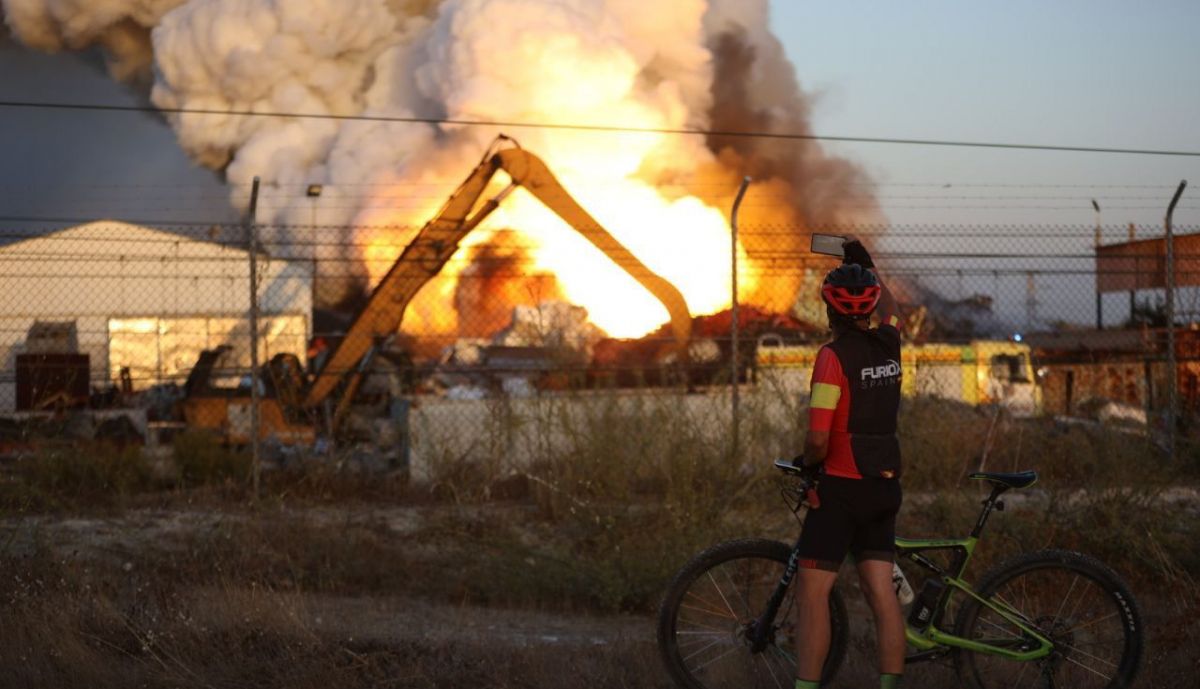 Un ciclista fotografía el incendio del desguace en El Portal, en Jerez.