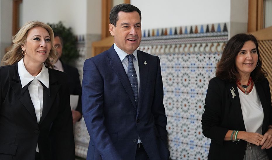Juanma Moreno, acompañado de las consejeras de Economía, Carolina España, y de Empleo, Rocío Blanco, en los pasillos del Parlamento de Andalucía. 