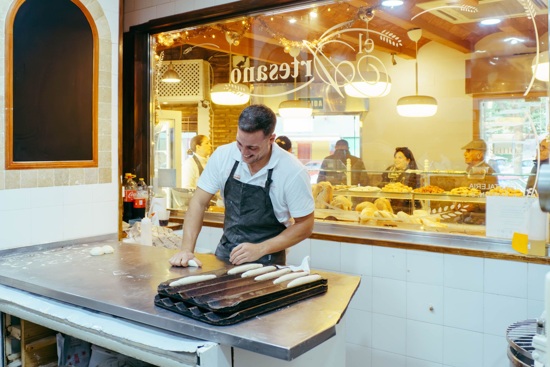 Un artesano amasando el pan, con la clientela de fondo.