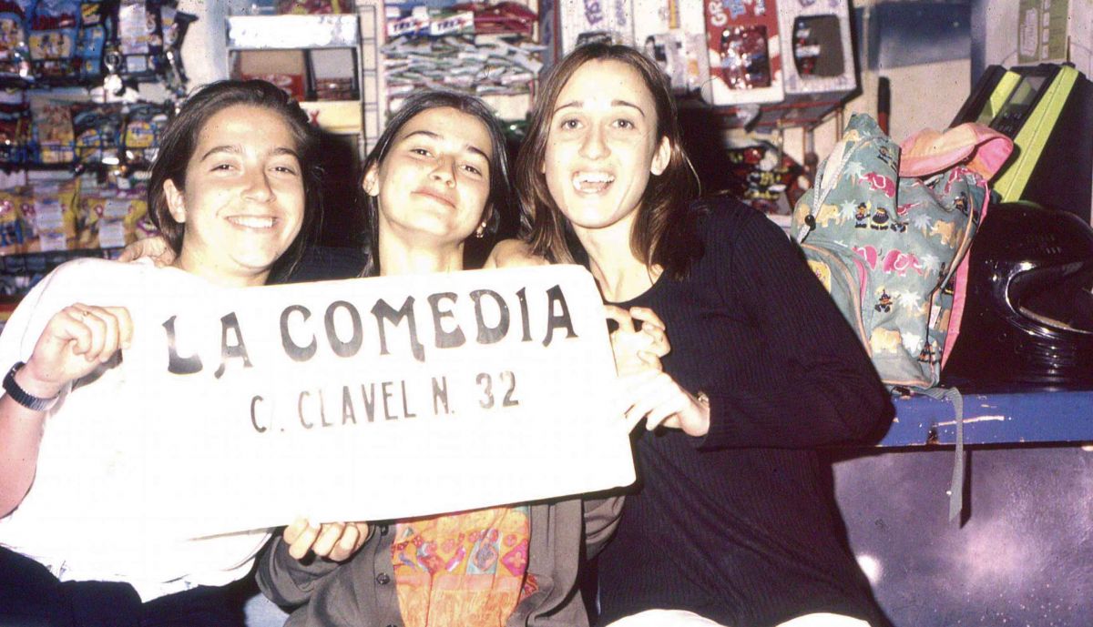 Tres jóvenes, con un cartel con la dirección de La Comedia.