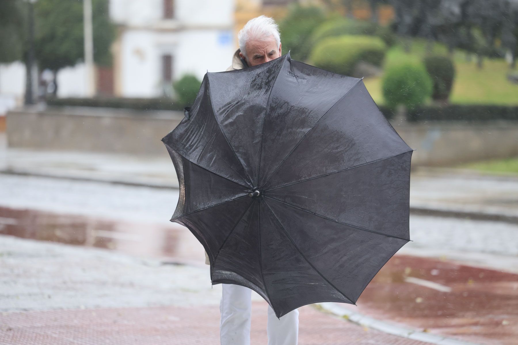 Un hombre intenta cerrar su paraguas un día de lluvia y viento.