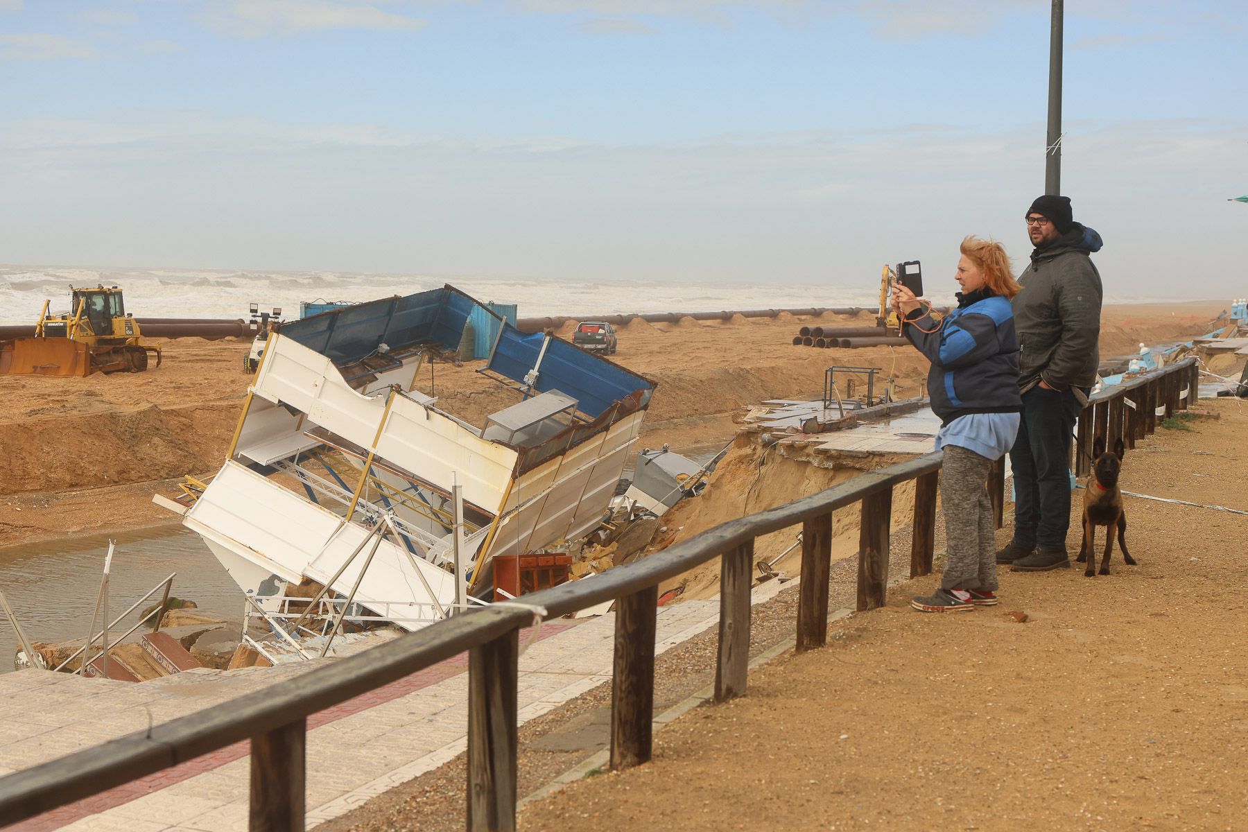 Vecinos de Matalascañas hacen fotos a los destrozos provocados por los temporales en el paseo marítimo.