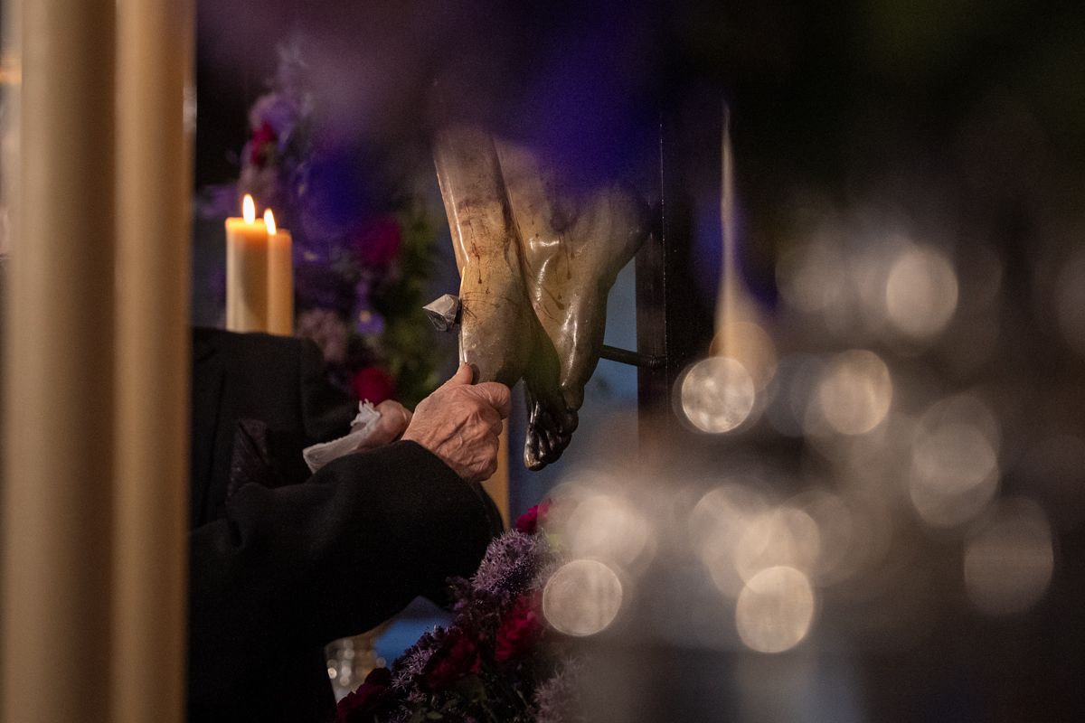 Unas manos ancianas tocando un pie del Crucificado 