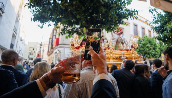 Un hombre toma una foto con el móvil al misterio de la Lanzada, cerveza en mano.
