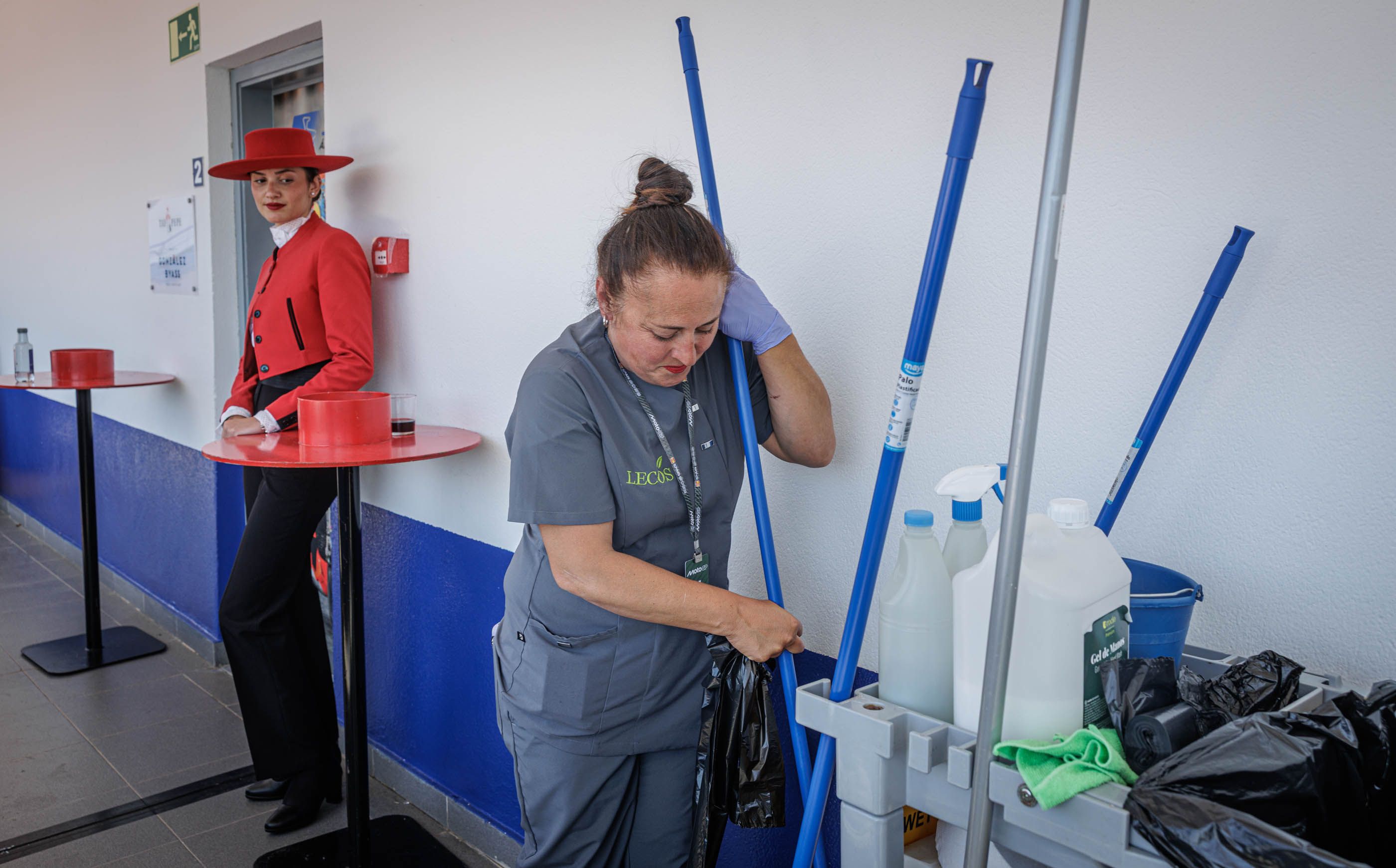 Una empleada de la limpieza ante la mirada de una chica Tío Pepe, en la zona de las 'mezzaninas' del Circuito de Jerez-Ángel Nieto, este domingo de carreras.