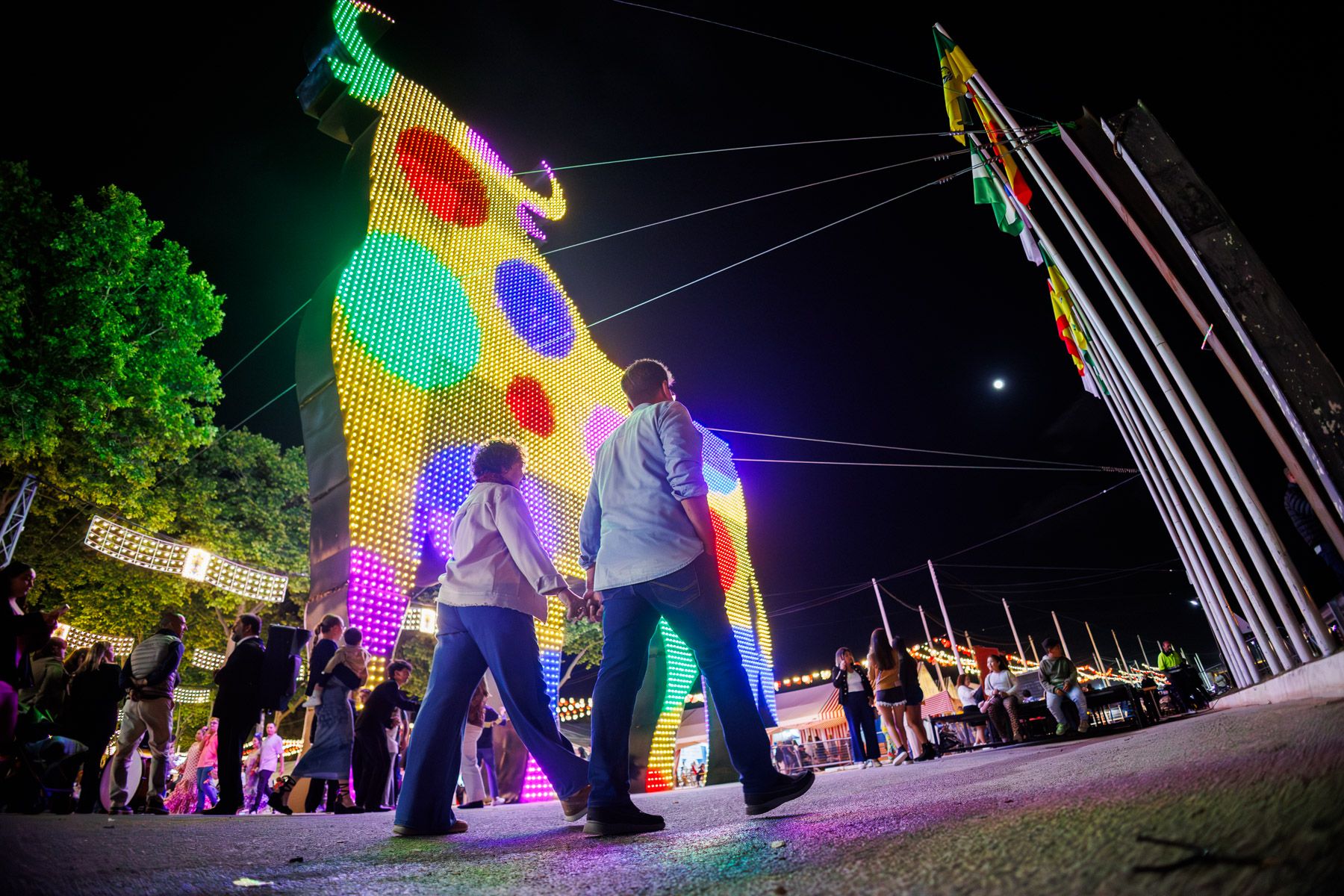 Personas caminan junto al ya clásico toro de la portada de la Feria de El Puerto. 