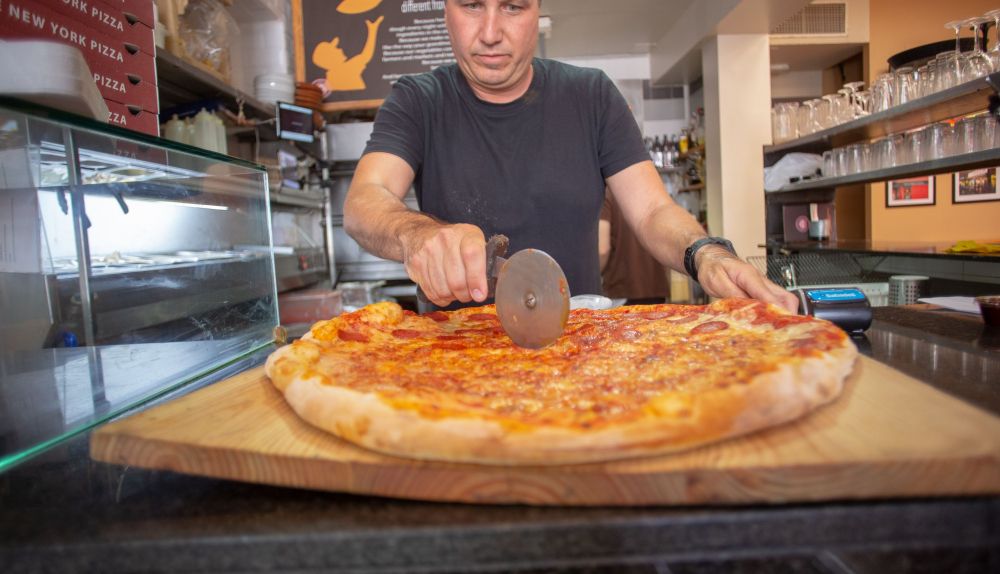 James Bem corta una porción de su pizza, en su local de Slice of New York en Rota. JUAN CARLOS TORO