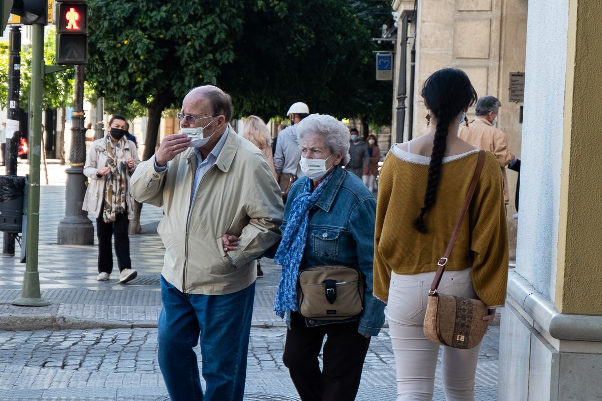 Una pareja de personas mayores, con mascarilla, andando por la calle.