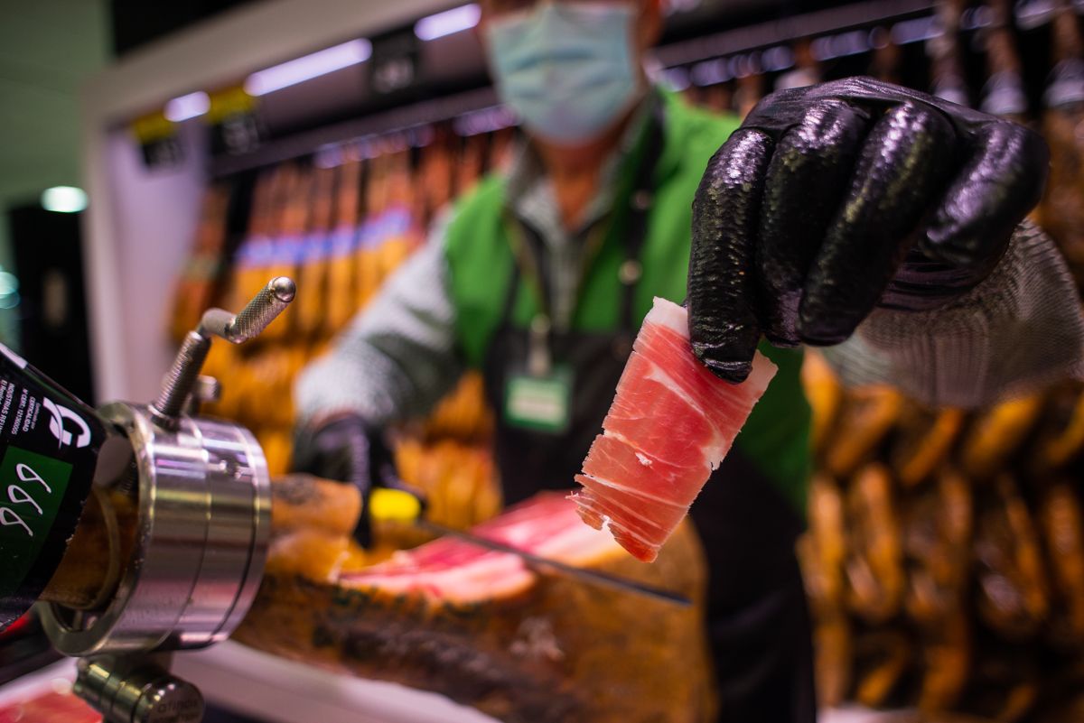 Un trabajador corta jamón en un supermercado.