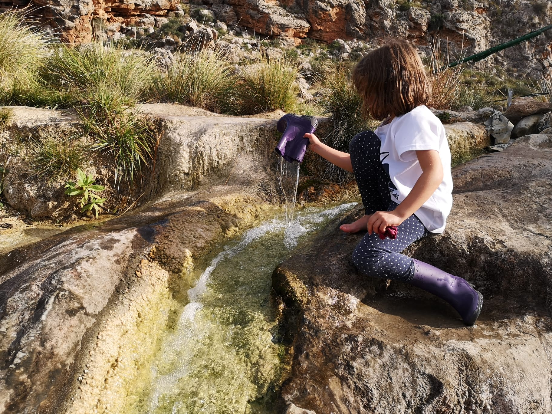 Escuchar llover. Una niña jugando con la bota de agua en una acequia, a falta de charcos de lluvia.