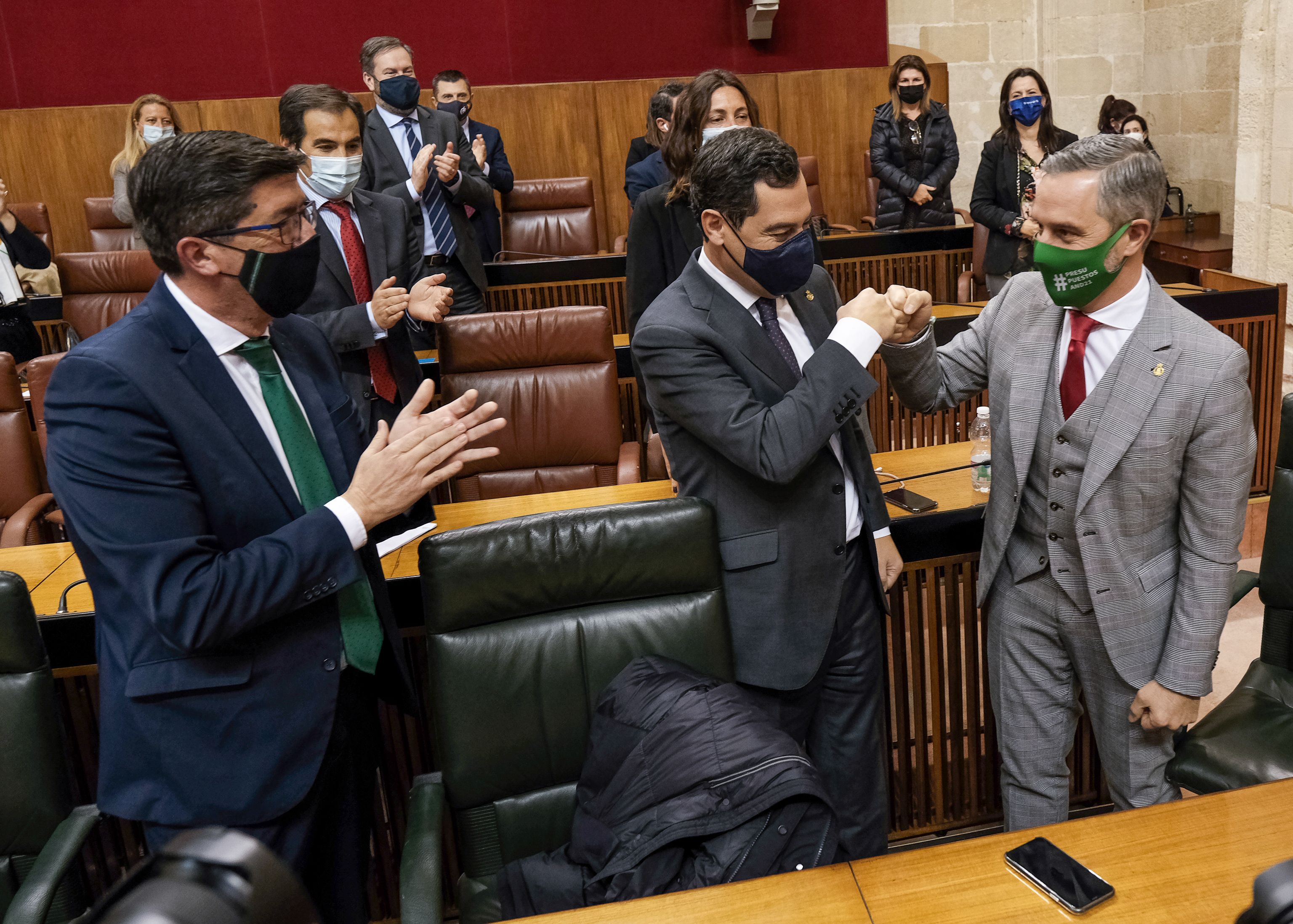 El presidente de la Junta de Andalucía, Juan Manuel Moreno, felicita al consejero de Hacienda, Juan Bravo, por la aprobación del Presupuesto, en presencia del vicepresidente, Juan Marín. Autor: Parlamento de Andalucía