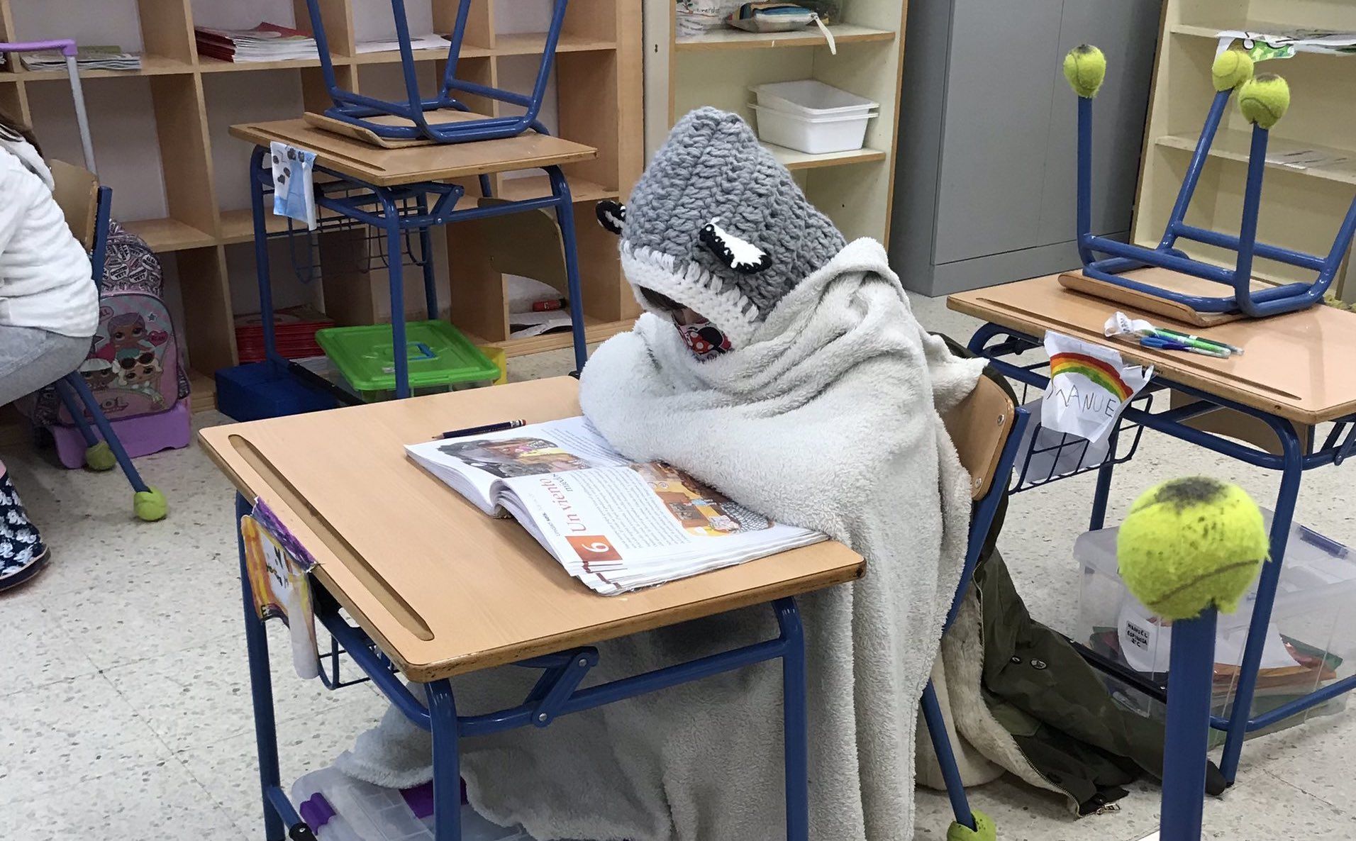 Un alumno se tapa con una manta por el frío que pasa en una aula andaluza.