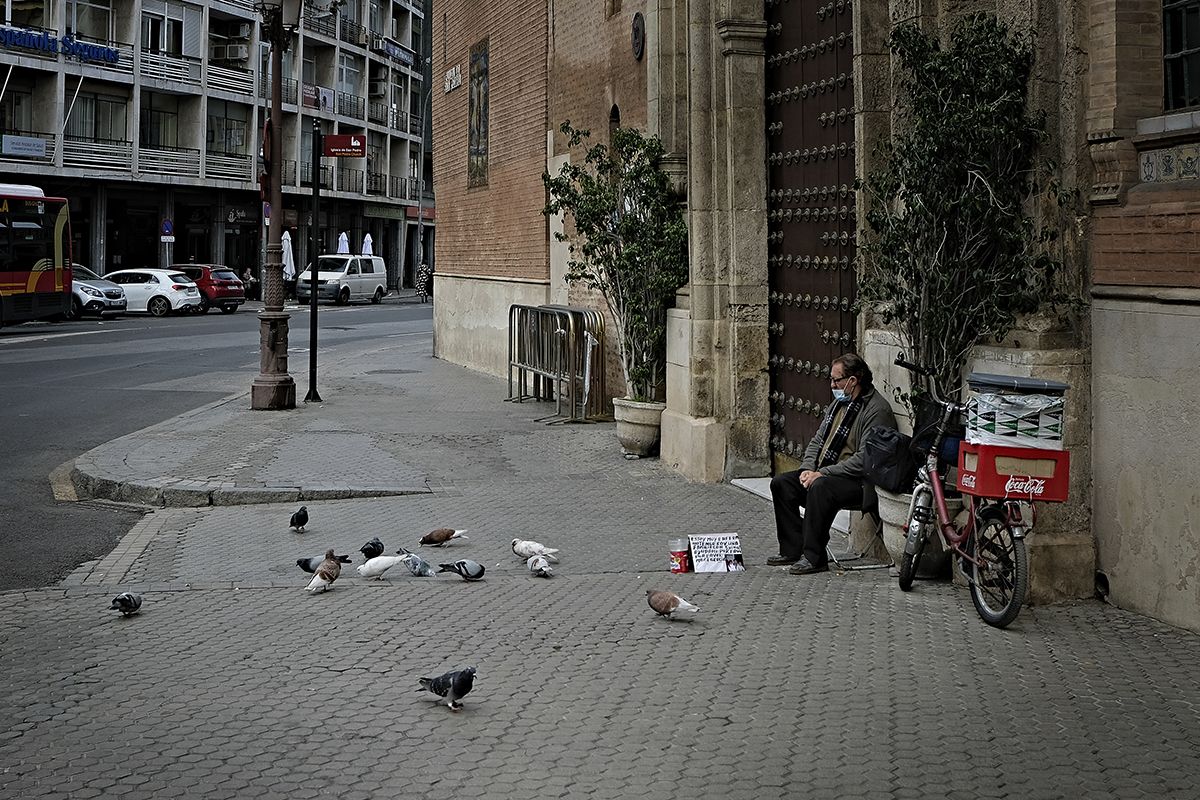 Un hombre echa de comer a las palomas sentado en la puerta de la parroquia de Santa Ángela de la Cruz.