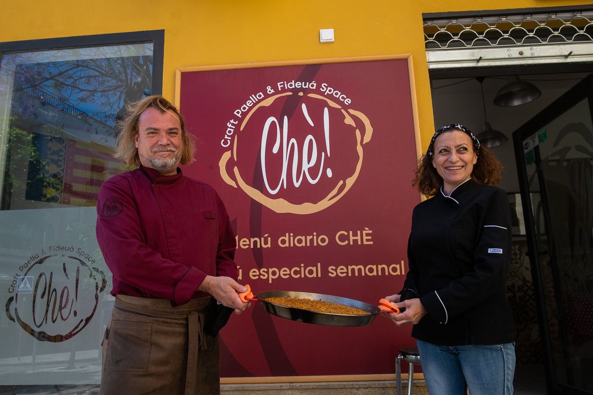 Carlos y María José con un 'rossejat' en la puerta del restaurante con cocina abierta y paellas valencianas.