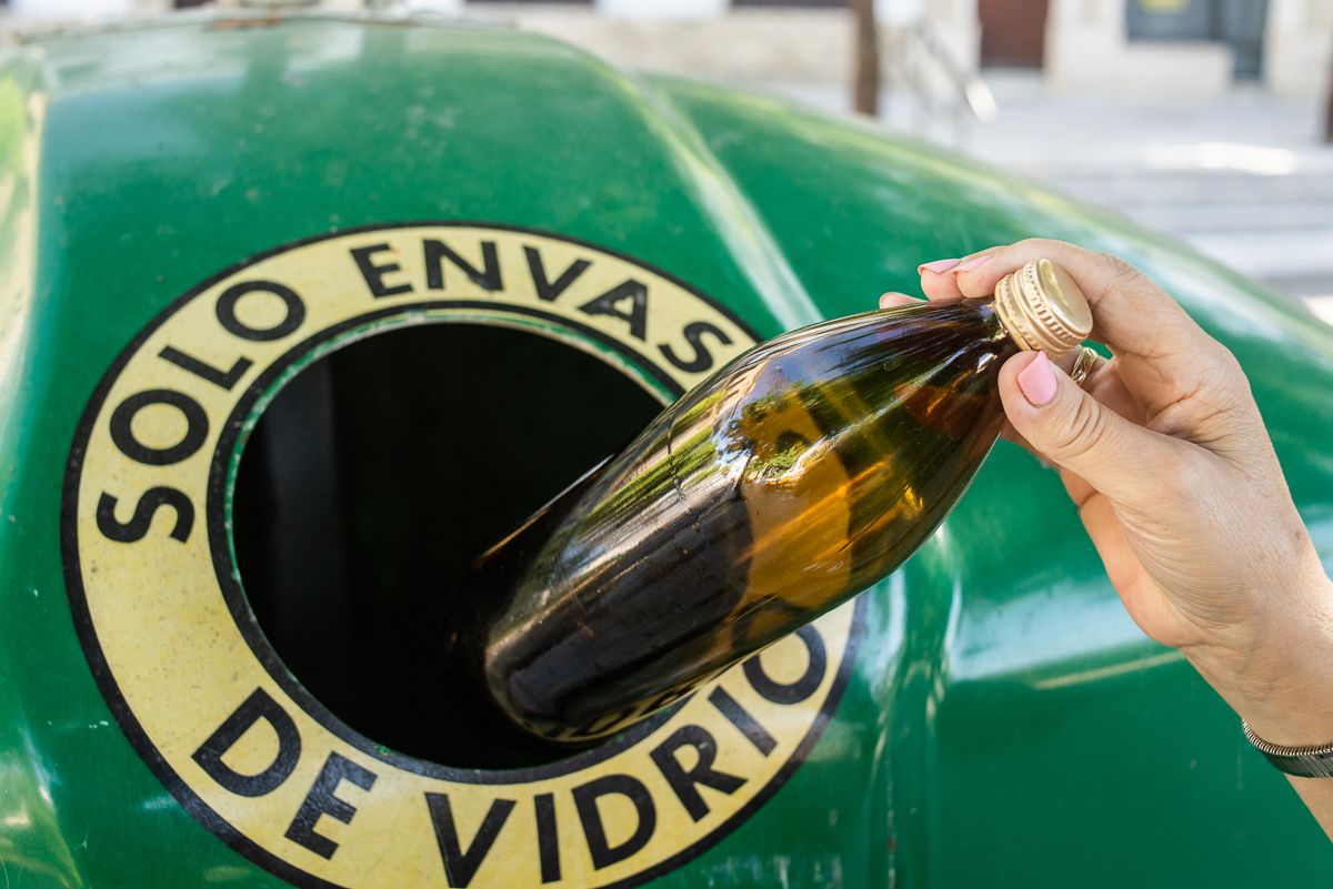 Una persona introduce una botella de vidrio en el contenedor verde para reciclar. 