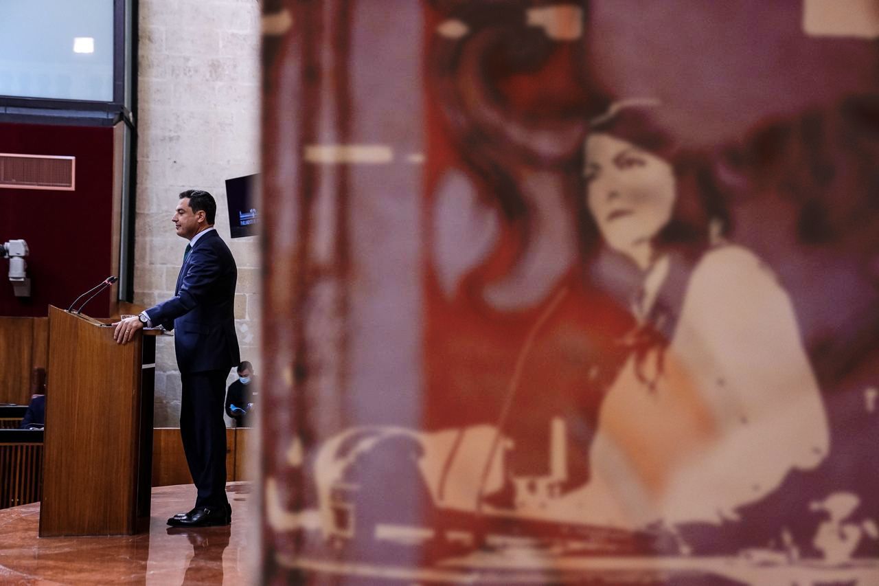 El presidente de la Junta, Juan Manuel Moreno, con la imagen de Macarena Olona, posible presidenciable de Vox, acechando.