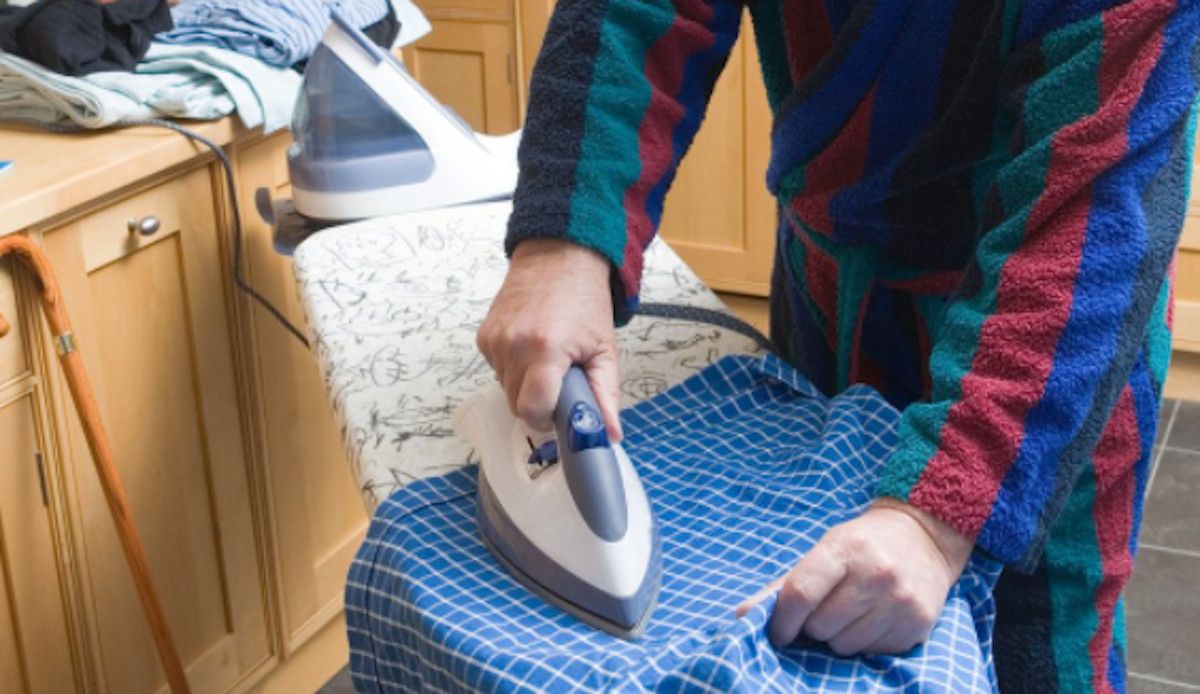 Un hombre plancha su camisa y participa en el trabajo doméstico para contribuir a la corresponsabilidad familiar.