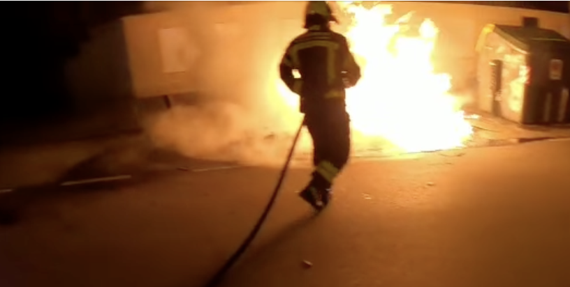 Un bombero, sofocando las llamas de contenedores quemados en Jerez.
