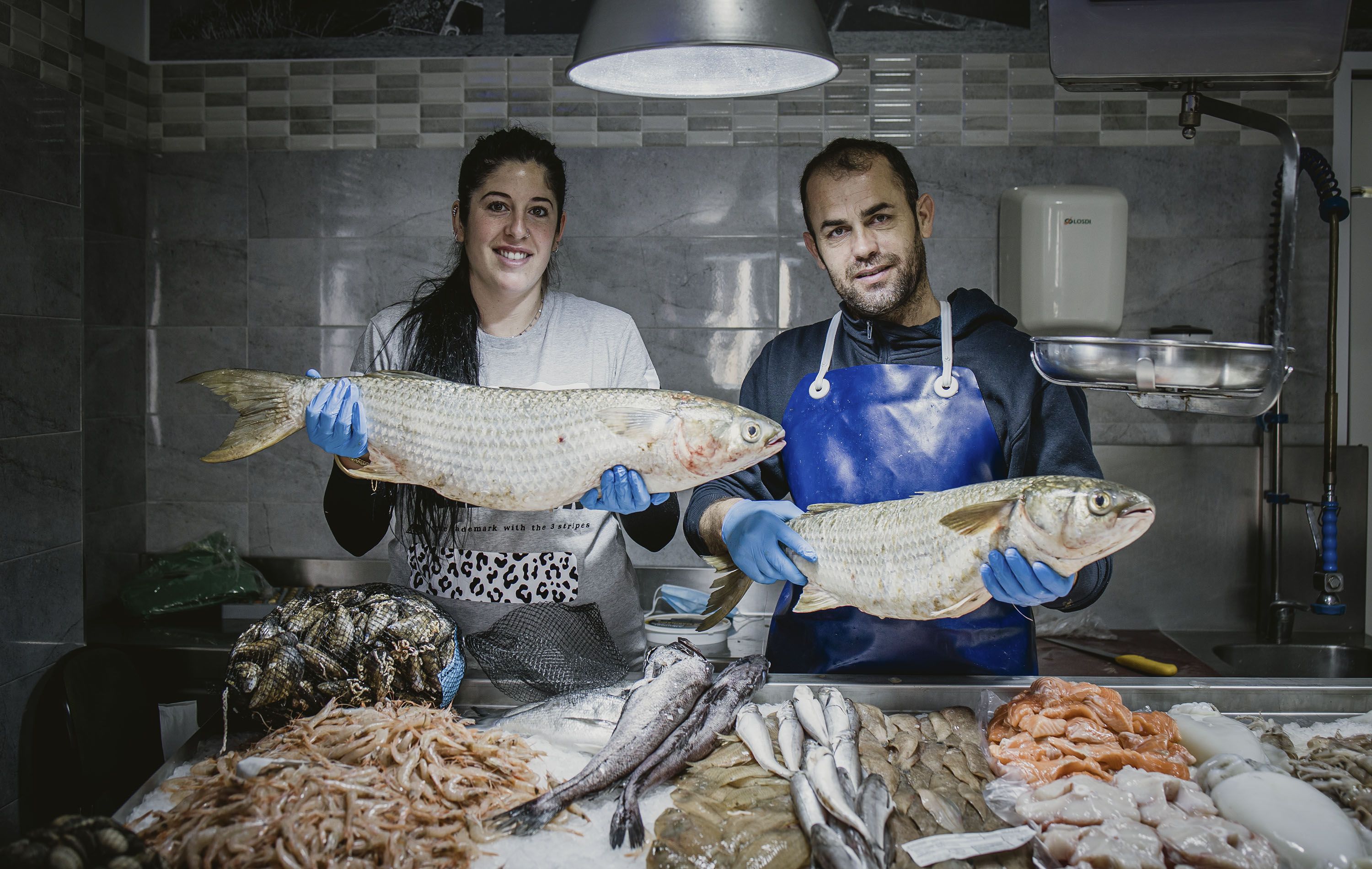 María Regla y David posan con dos albures, tras el mostrador de su céntrica pescadería en Trebujena.
