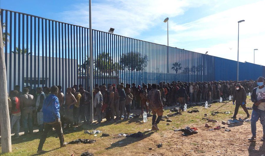 Personas en fila a lo largo de la valla de Melilla.