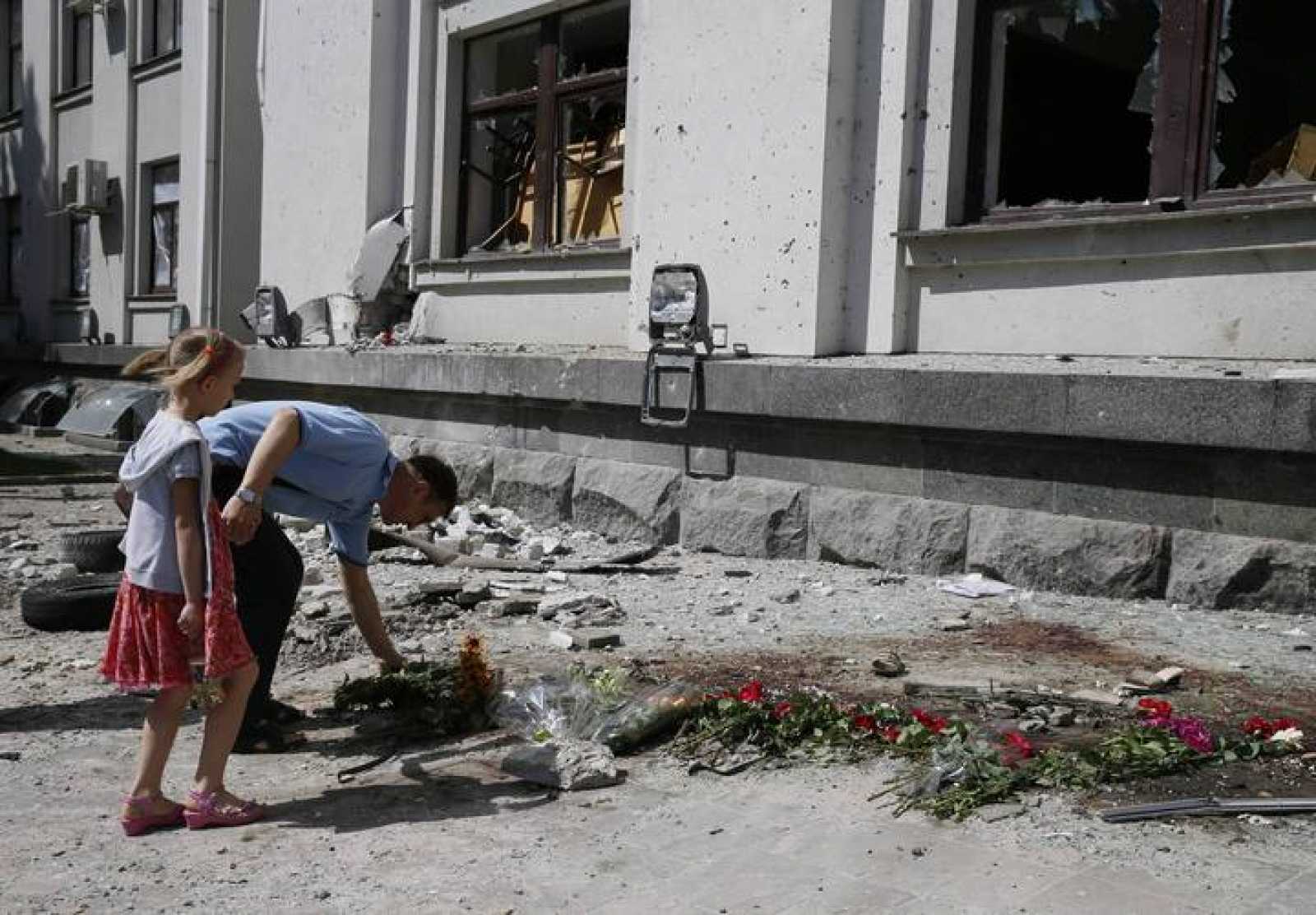 Un padre y su hija colocan flores en Ucrania en un lugar donde han perdido la vida varias personas.